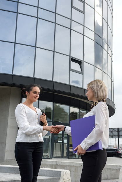 Twee zakelijke vrouwen in pakken handshaking voordat kantoorgebouw