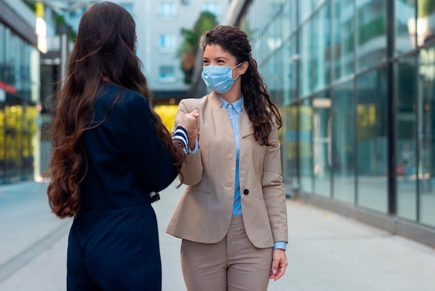 Twee zakenvrouwen die maskers dragen en buiten met vuisten stoten