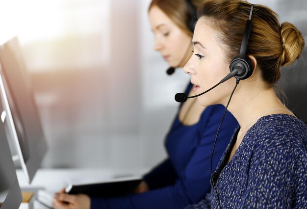 Foto twee zakenvrouwen hebben gesprekken met de klanten via headsets, terwijl ze aan het bureau zitten in een zonnig modern kantoor. diverse mensengroep in een callcenter. telemarketing en klantenservice.