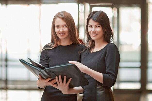 Twee zakenvrouwen lezen zakelijke documenten die in de kantoorlobby staan.