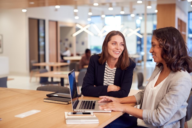 Twee zakenvrouwen met laptop aan balie in open kantoor werken samen aan project