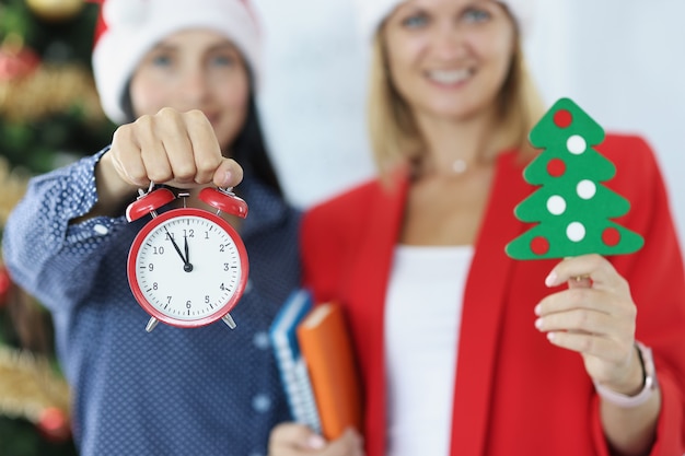 Twee zakenvrouwen met rode wekker en kerstboom nieuwjaar en kerstviering