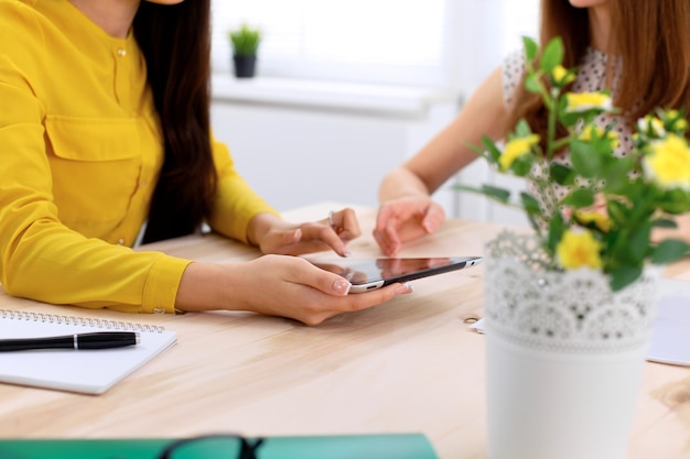 Twee zakenvrouwen of vrienden praten en gebruiken tabletcomputer.