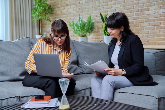 Twee zakenvrouwen zitten op de bank in het kantoor en praten over werk.