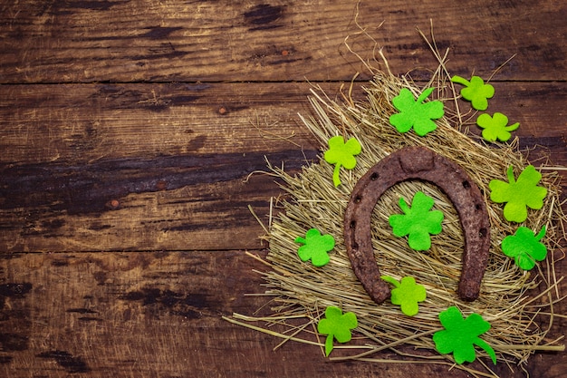 Twee zeer oude gietijzeren metalen paardenhoeven op hooi, klavervilt blad. Veel geluk symbool, St.Patrick's Day concept. Antieke houten achtergrond, paard accessoires