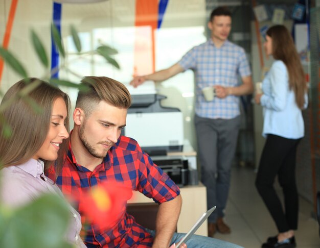 Twee zelfverzekerde jonge mensen die naar het touchpad kijken terwijl hun collega's op de achtergrond werken