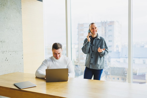 Twee zelfverzekerde jonge mensen zitten samen aan een tafel en een van hen wijst naar een laptop Werk aan een nieuw project Succesvolle collega's die samenwerken op kantoor