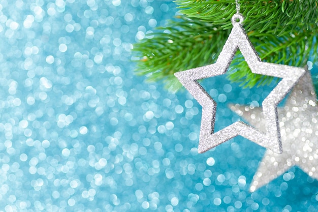 Twee zilveren ster op een kerstboomtak op een blauwe achtergrond van bokeh schijnt.