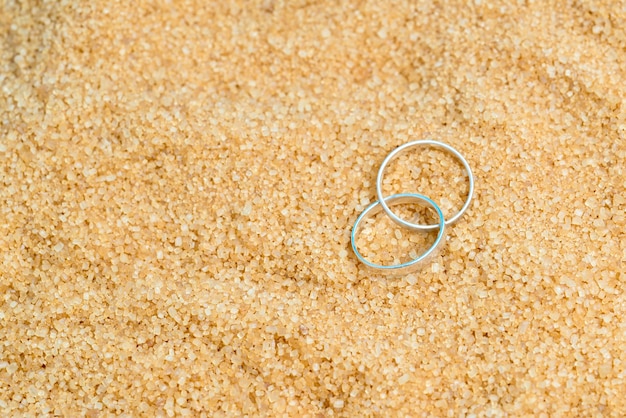 Twee zilveren trouwringen in het zand op de achtergrond van strand en zee