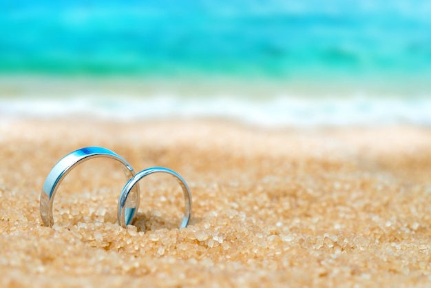 Twee zilveren trouwringen in het zand op de achtergrond van strand en zee