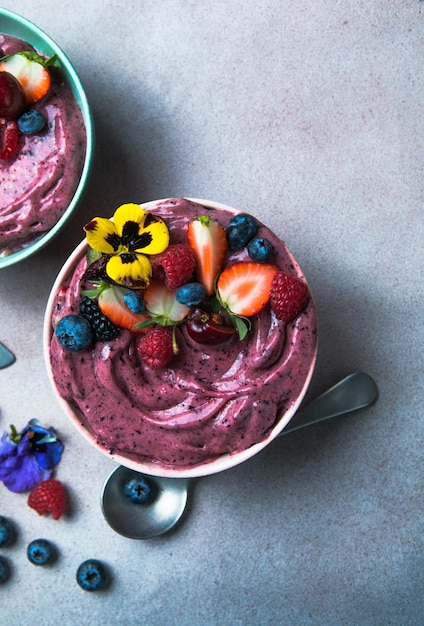 Twee zomerse acai smoothie kommen met aardbeien bosbessen op grijze betonnen achtergrond ontbijtkom met fruit en ontbijtgranen close-up bovenaanzicht gezonde voeding