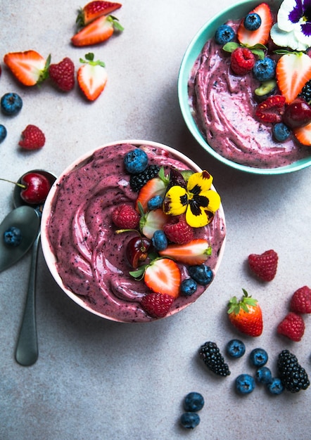 Twee zomerse acai smoothie kommen met aardbeien bosbessen op grijze betonnen achtergrond Ontbijtkom met fruit en ontbijtgranen close-up bovenaanzicht gezonde voeding