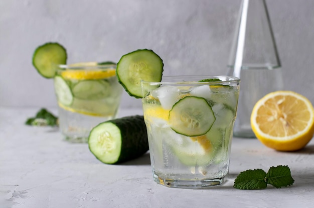 Twee zomerse verse ijsdranken met muntcitroen en komkommer plus een fles mineraalwater gezonde mojito-detoxcocktail op grijze achtergrond