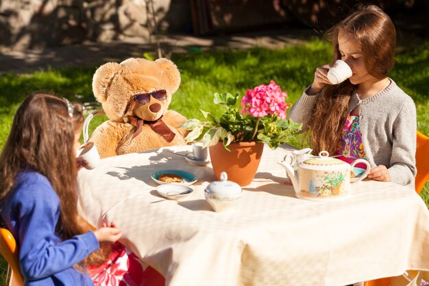 Twee zusjes die engels ontbijten met teddybeer op het erf