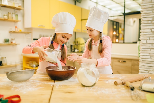 Twee zusjes koken in doppen giet bloem in een kom, koekjes voorbereiding op de keuken. Kinderen koken gebak, kinderen chef-koks maakt deeg, kind voorbereiding van cake