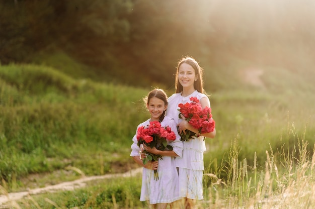 Twee zussen gekleed in witte jurken hebben samen leuke zomer. Meisjes houden bloemen vast.