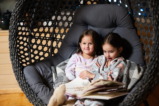 Twee zussen in pyjama's en gebreide sokken in een comfortabele hangstoel die boeken leest in een gezellig houten huisje in een huisje Leven op het platteland