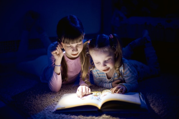 Twee zussen lezen van een boek met een zaklamp in een donkere kamer 's nachts