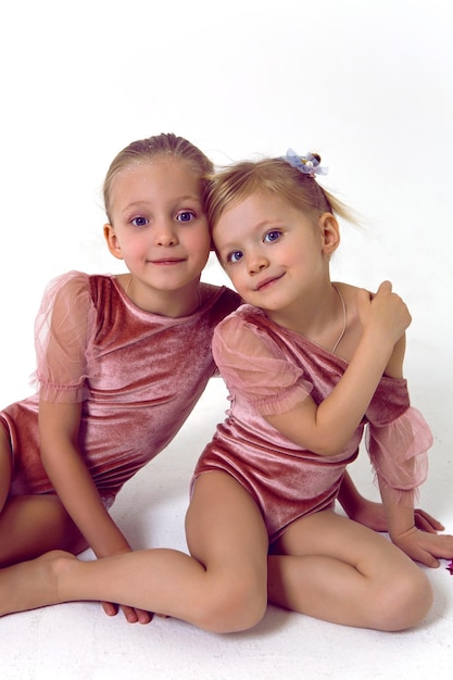 Foto twee zussen meisje zit op een witte achtergrond in roze bodysuits