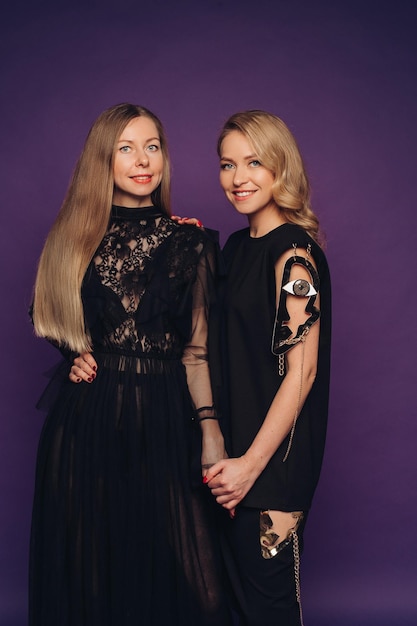 Twee zussen poseren in de studio op een paarse achtergrond 2 mooie vrouwen in zwarte kostuums verzameld voor een feestje