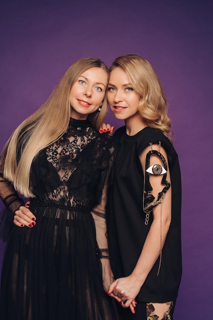 Twee zussen poseren in de studio op een paarse achtergrond 2 mooie vrouwen in zwarte kostuums verzameld voor een feestje