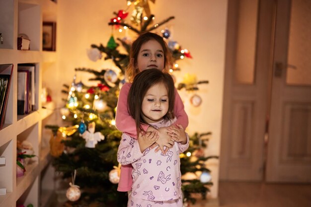 Twee zussen samen in de buurt van de kerstboom 's avonds thuis