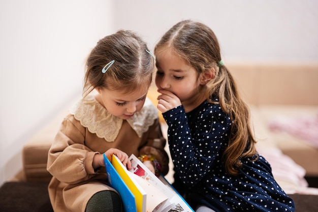 Twee zussen zitten op een bank en lezen samen een boek