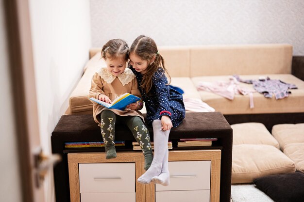 Twee zussen zitten op een bank en lezen samen een boek