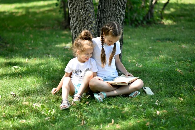 Twee zustermeisjes zitten op groen gras en lezen een boek Education Childhood