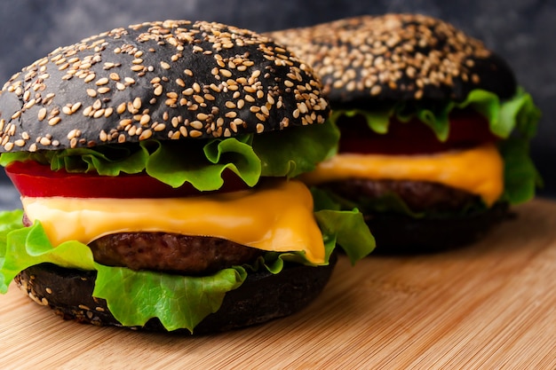 Twee zwarte hamburgers met sesamzaad zwart broodje, rundvlees kotelet, kaas en groenten op houten rustieke snijplank tafel. Detailopname. Selectieve zachte focus. Tekst kopie ruimte