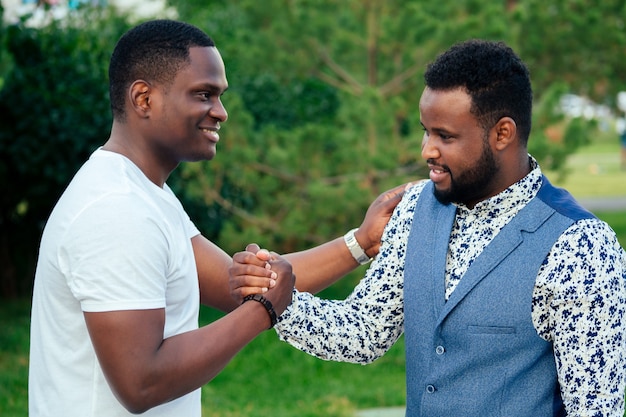 Twee zwarte mannen in stijlvolle pakken ontmoeten elkaar in een zomerpark. Afro-Amerikanen vrienden Spaanse zakenman begroeten elkaar teamwerk buitenshuis