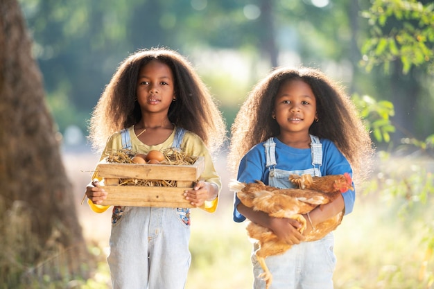 Foto twee zwarte meisjes houden een bruine kip in hun omhelzing van liefde met hun ogen dicht een klein zwart meisje houdt een kip vast in een boerderij