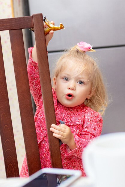 Tweejarig blond meisje speelt bij een stoel in de keuken