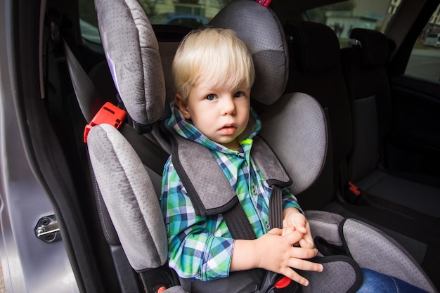 Tweejarige jongen zit in een autostoeltje en kijkt naar de camera Ernstige jongen zit vastgemaakt in de auto