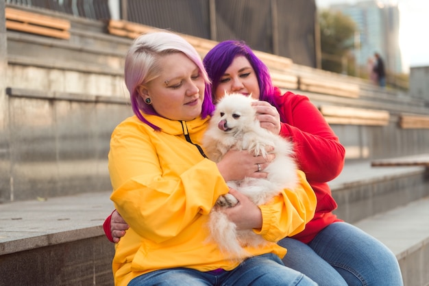 tweekleurige haar lesbische vrouw zittend op een bankje buiten met schattige hond spitz