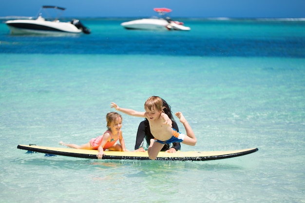 Tweeling, jongen en meisje met moeder surfen in de oceaan op een schoolbord