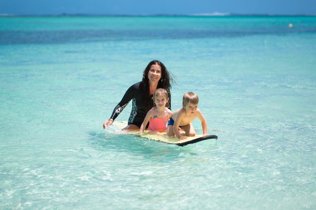 Tweeling, jongen en meisje met moeder surfen in de oceaan op een schoolbord
