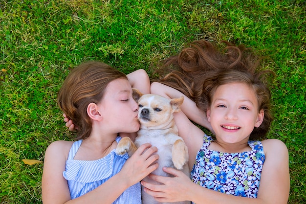 tweelingzusjes spelen met chihuahua hond liggend op het gazon