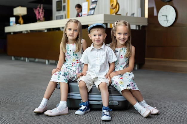 Tweelingzussen en broer zittend op een koffer in een hotel