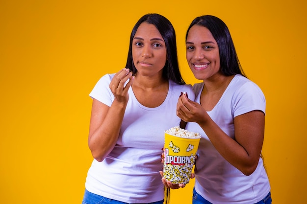 Tweelingzussen op gele achtergrond die popcorn eten