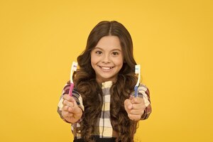 Tweemaal sneller meisje schattig lang haar houdt tandenborstels gele achtergrond kind meisje houdt twee tandenborstels kind schoolmeisje slim kind blij gezicht zorgen hygiëne tanden poetsen concept tandenhygiëne