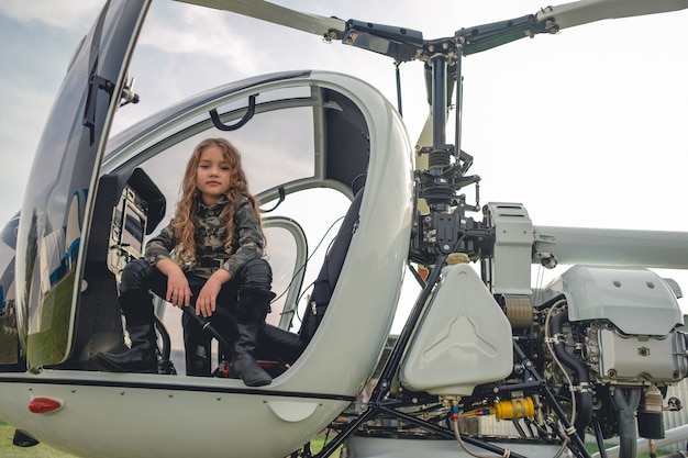 Tween girl in camouflage style tunic sitting in open helicopter cockpit