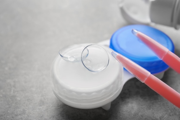 Tweezers and contact lenses with container on gray background