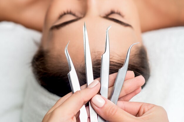 Tweezers for eyelash extensions above the head of young woman, close up.