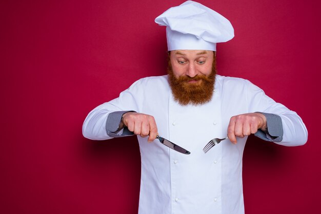 Twijfelchef met baard en rood schort houdt bestek in de hand