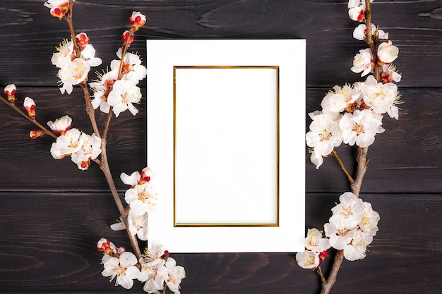 Twijgen van de abrikozenboom met bloemen en wit fotokader op houten achtergrond.