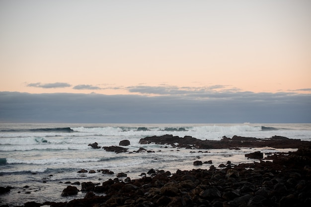 Twilight over the waving sea coast with wild stones on windy evening under the sky