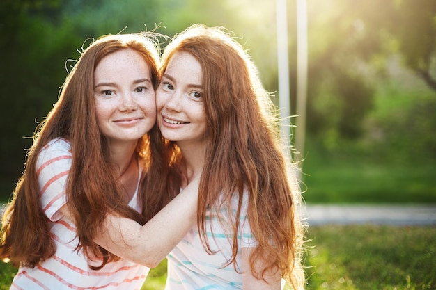 Twin ginger sisters are best friends forever Young ladies looking at camera smiling on a sunny summer day Friendship concept