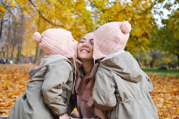 쌍둥이 소녀는 어머니에게 키스한다 그녀의 쌍둥이 딸과 함께 행복한 어머니는 담요에 앉아 시간을 보낸다