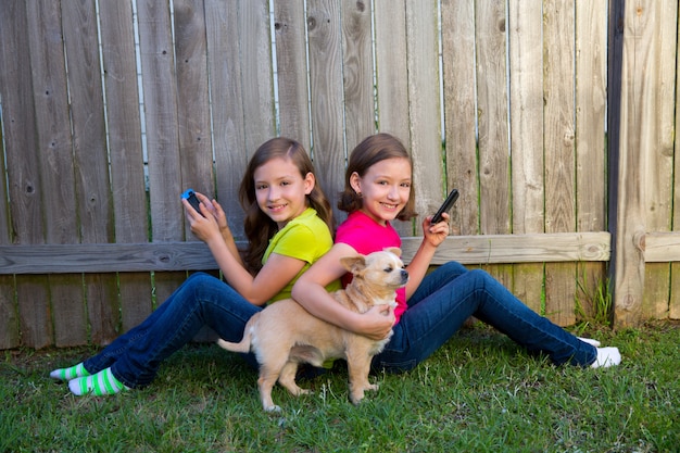 スマートフォンとチワワ犬を遊ぶ双子の姉妹の女の子